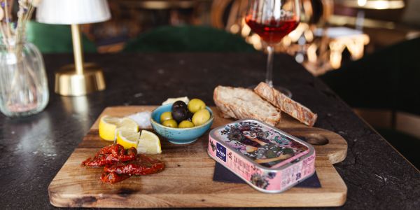 Sardinen, in der Dose serviert, mit Zitronenstücken, Oliven, getrockneten Tomaten, Brot  und Wein.