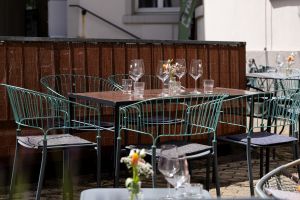 Holztisch mit türkisfarbenen Stühlen, platziert vor einem braunen Sichtschutzzaun aus Holz im sonnigen Innenhof.