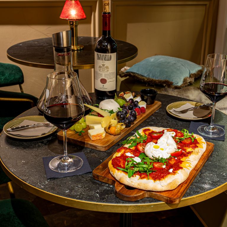 Reichhaltig gedeckter runder Tisch mit Pinsa Obst, Käse und Rotwein.